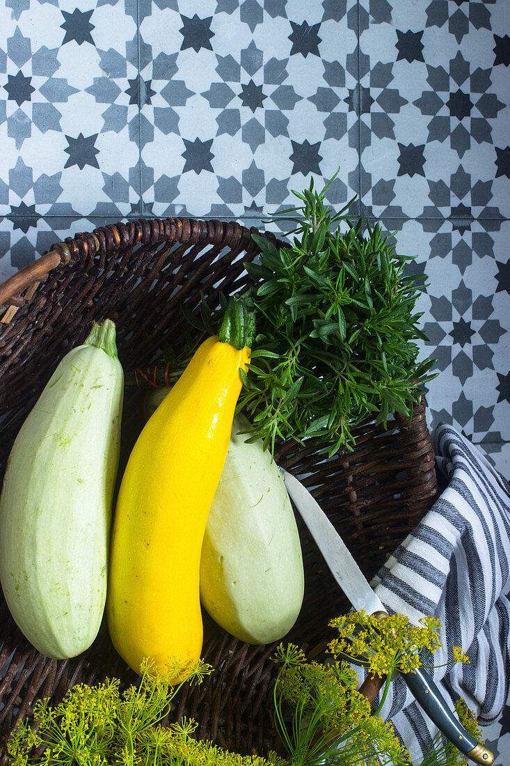 Various courgettes in a basket with fresh herbs