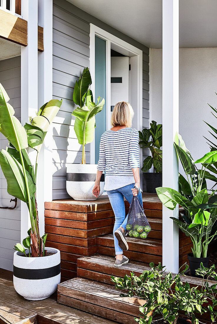 Veranda with wooden steps surrounded by foliage plants; woman carrying shopping bag