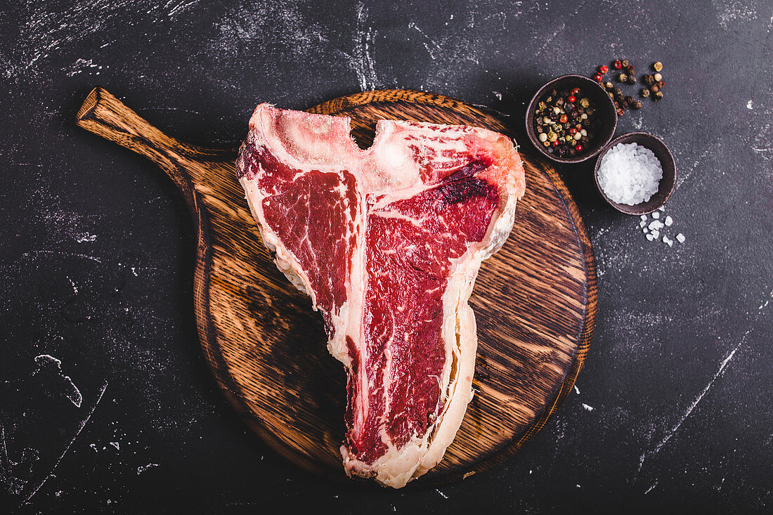 A raw T-bone steak on a wooden board (seen from above)