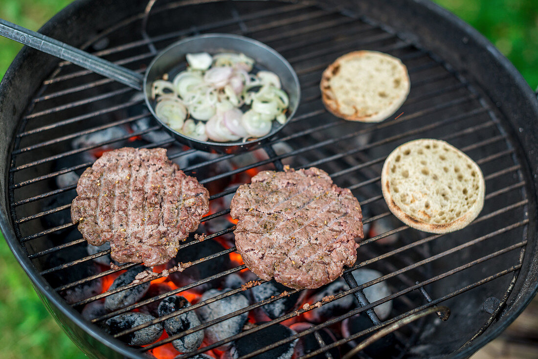 Burgerpatties, Burgerbrötchen und Pfännchen mit Zwiebelringen auf Grill