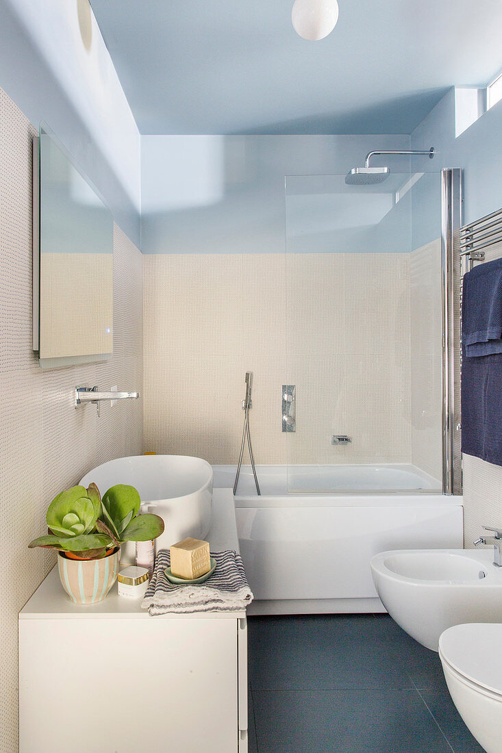 Waschtisch mit Aufsatzbecken und Badewanne im Bad mit hellen Wandfliesen und himmelblauer Decke