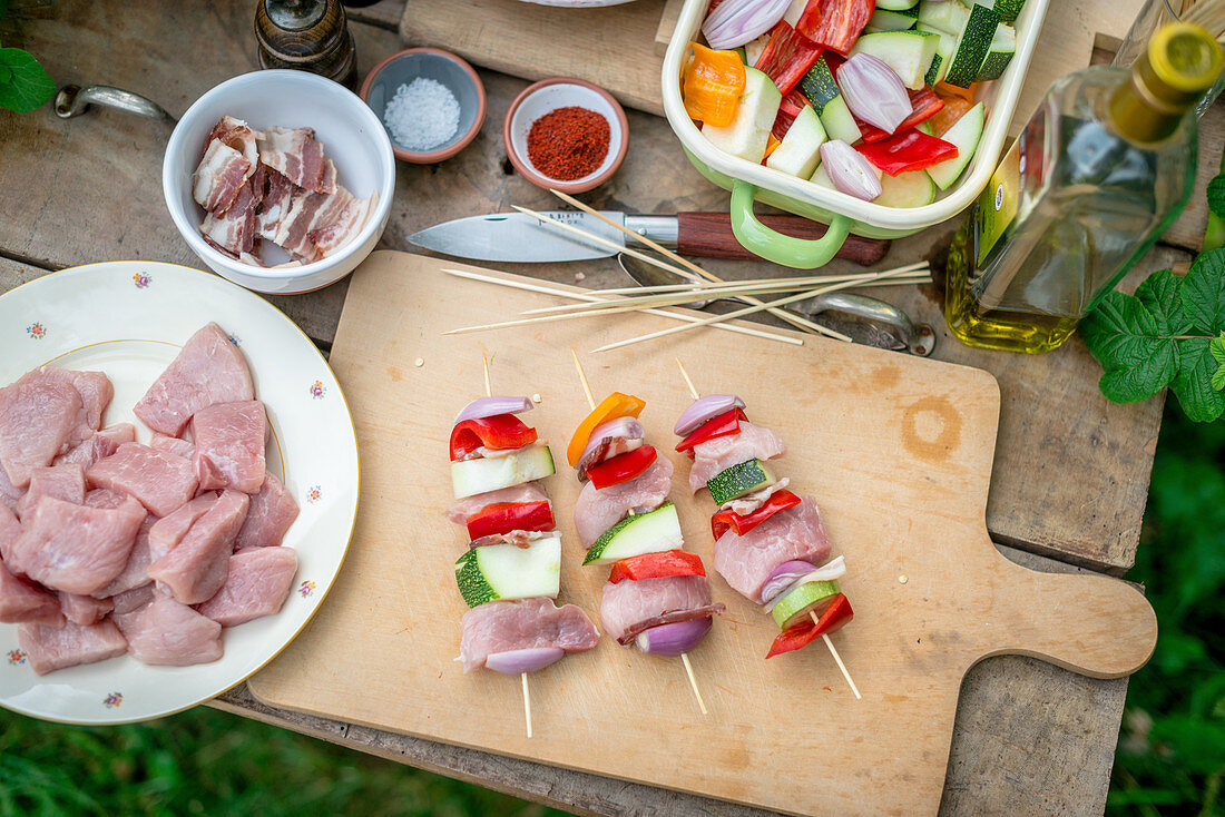 Rohe Fleischspieße mit Schweinefleisch, Speck und Gemüse auf Holzschneidebrett