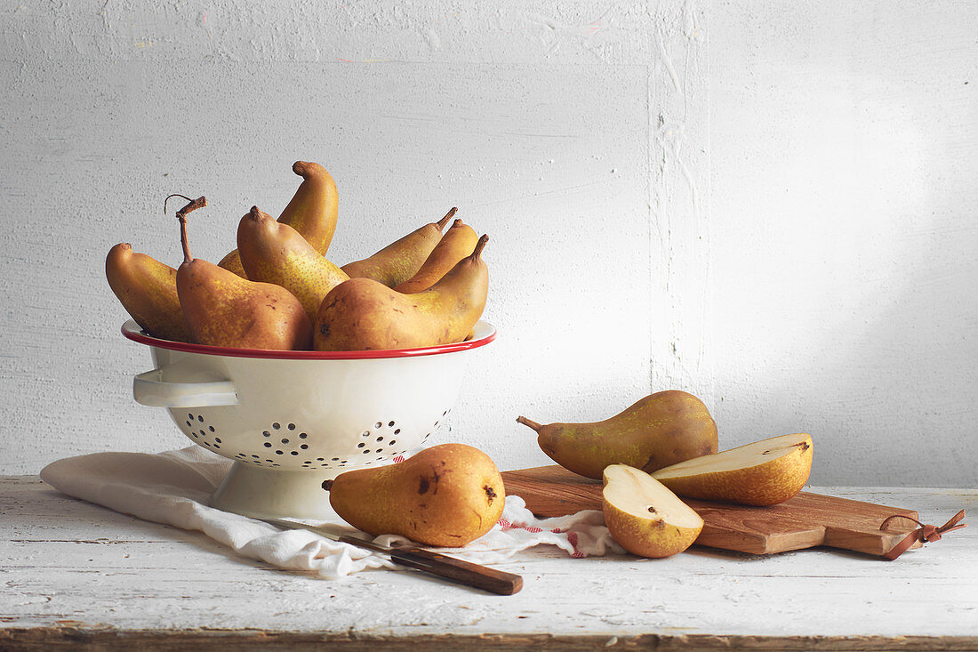 Conference pears in a colander and sliced on a wooden board
