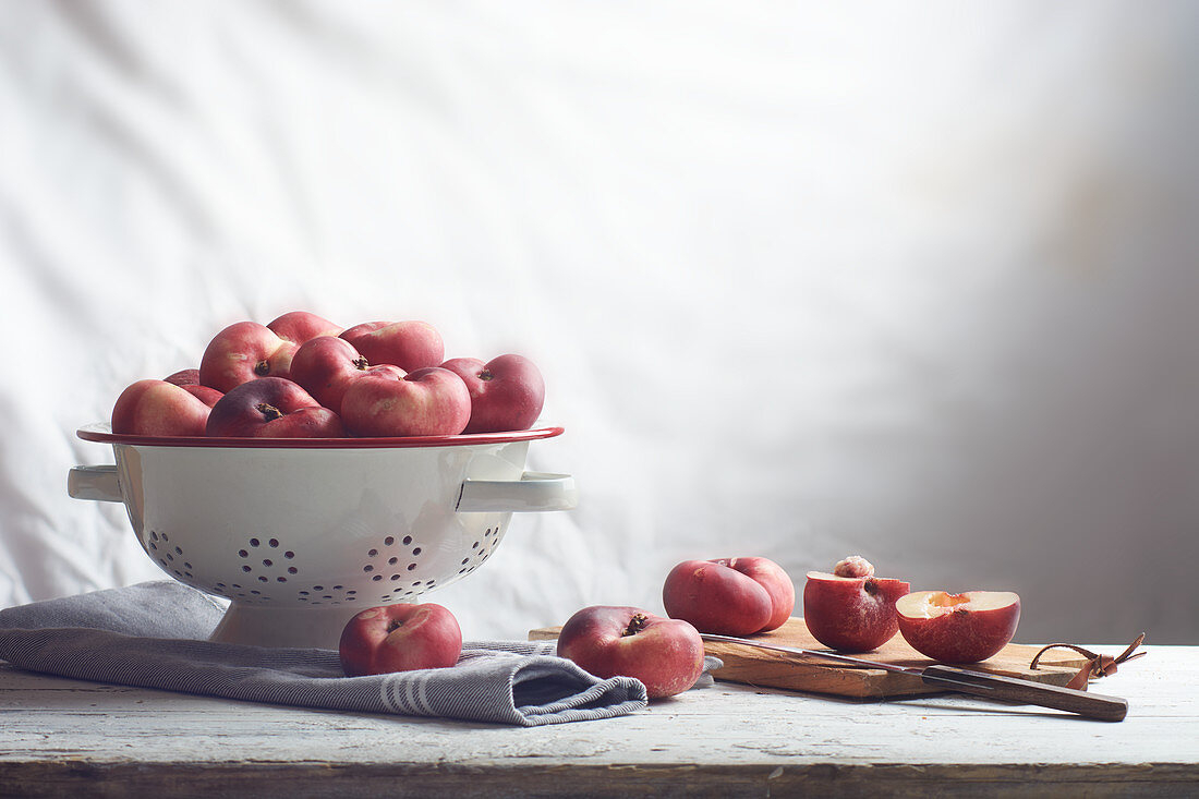 Flat nectarines in a colander and slices on a wooden board