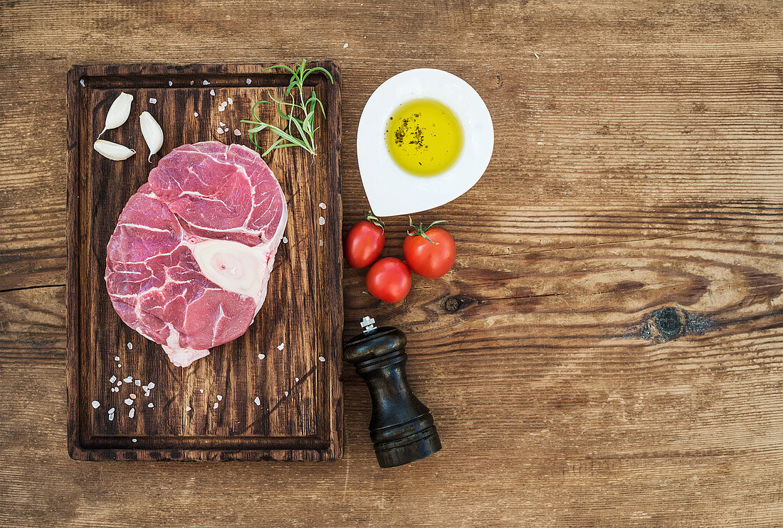 Cross cut for ossobuco cut with garlic cloves, cherry tomatoes, rosemary, pepper, oil and salt