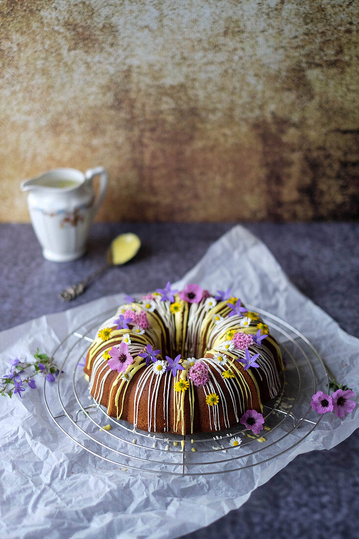 A guglhupf with yellow and white icing and edible flowers