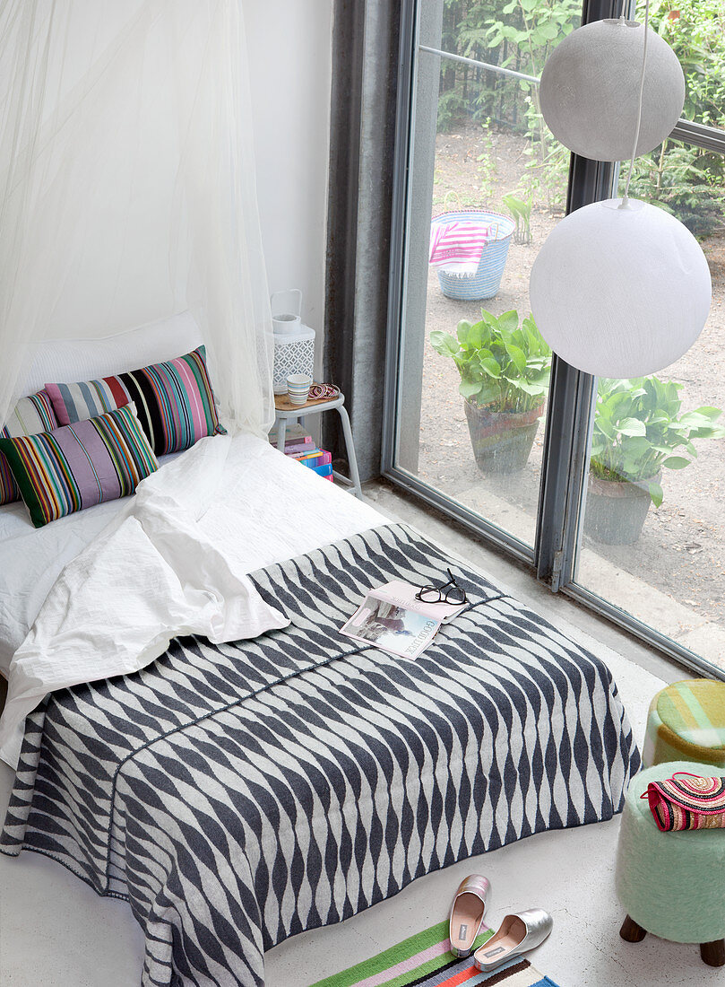 Black-and-white patterned bedspread and brightly striped pillows on double bed next to terrace doors