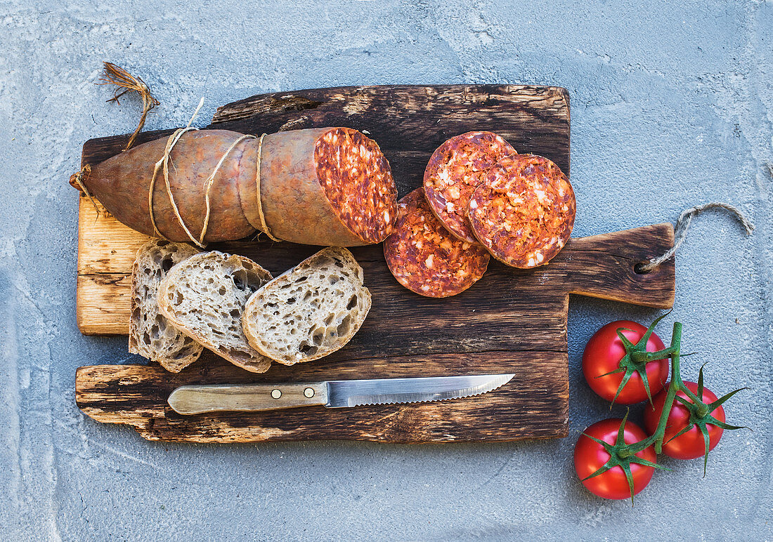 Wine snack set. Hungarian mangalica pork salami sausage, rustic bread and fresh tomatoes on dark wooden board