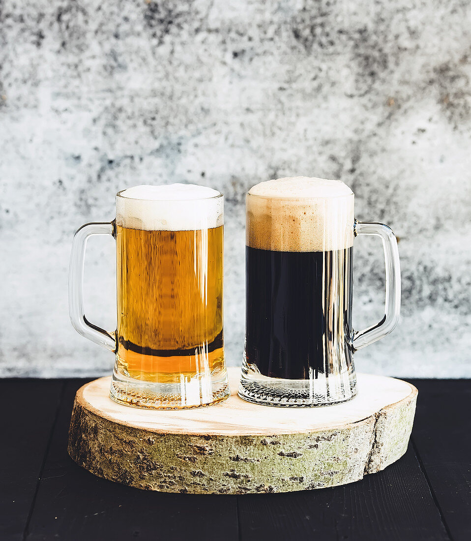 Light and dark beer in mugs on wooden board, grunge backdrop