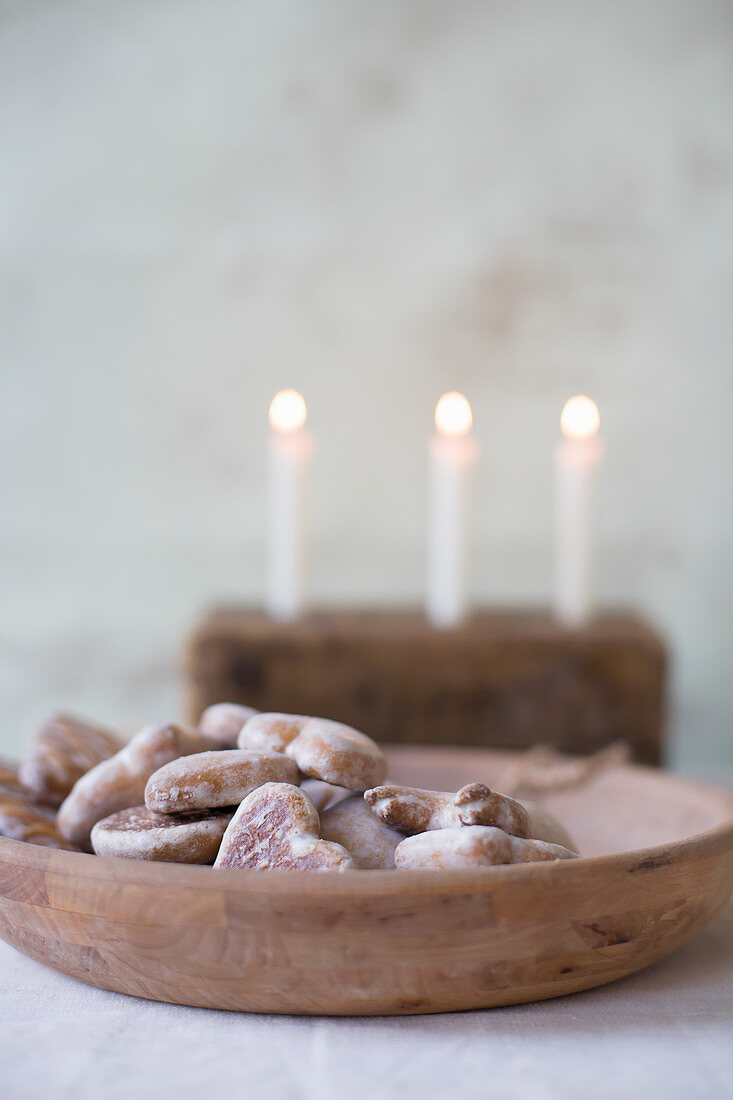Gingerbread hearts in wooden bowl in front of three lit candles