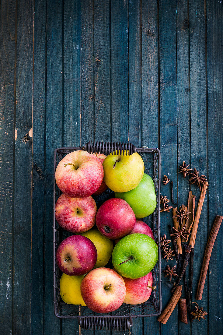 Verschiedene Äpfel im Drahtkorb und Gewürze auf blauem Holzuntergrund