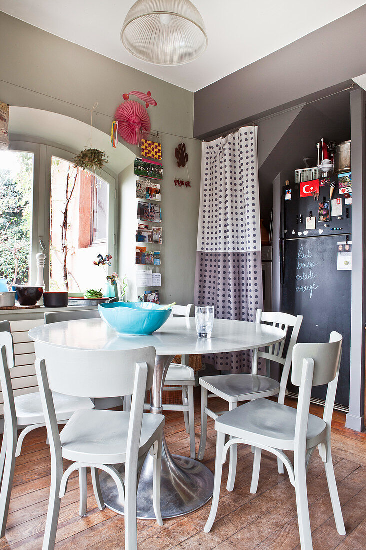 Round table, wooden chairs and fridge with chalkboard paint in niche in kitchen