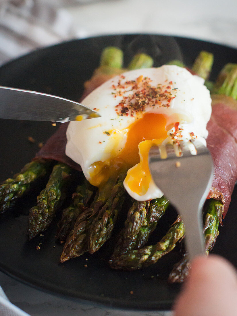 Grilled green asparagus wrapped in ham with a poached egg