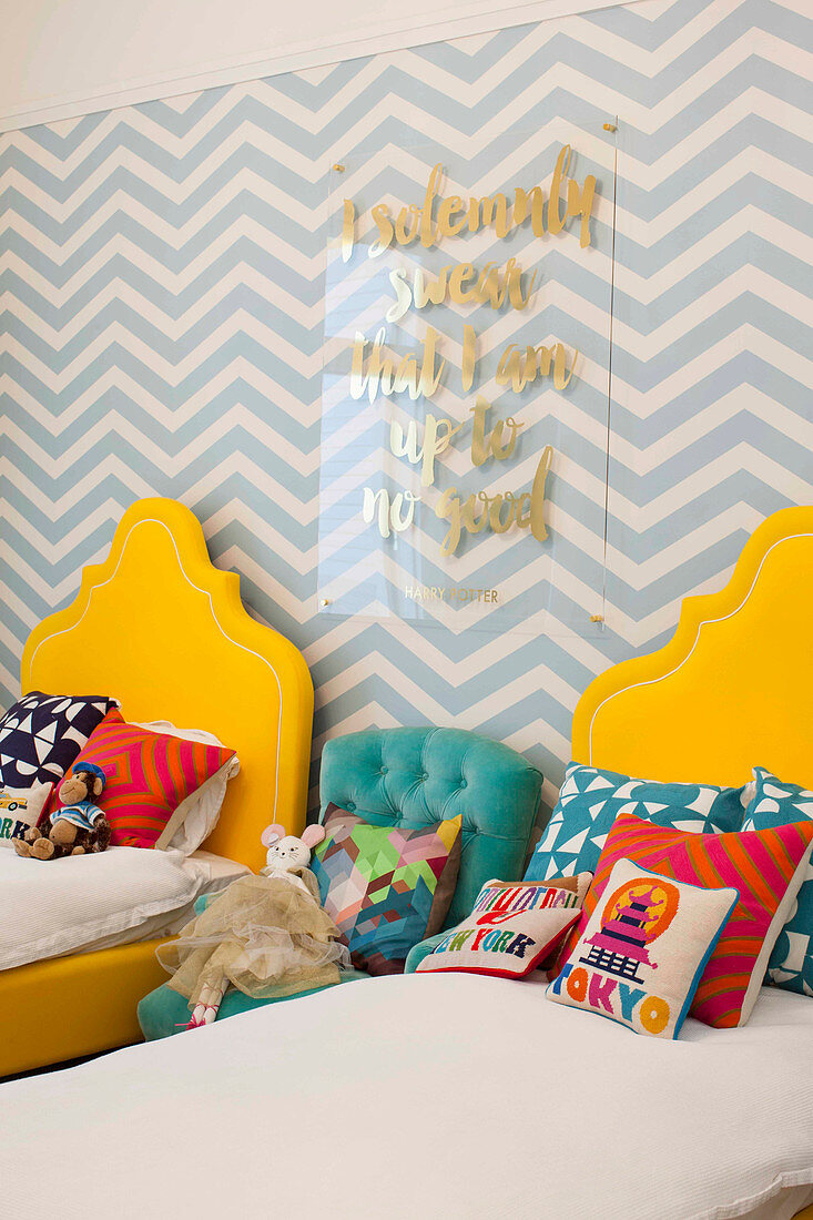 Two yellow beds with pillows and soft toys, zig-zag wallpaper and message on the wall