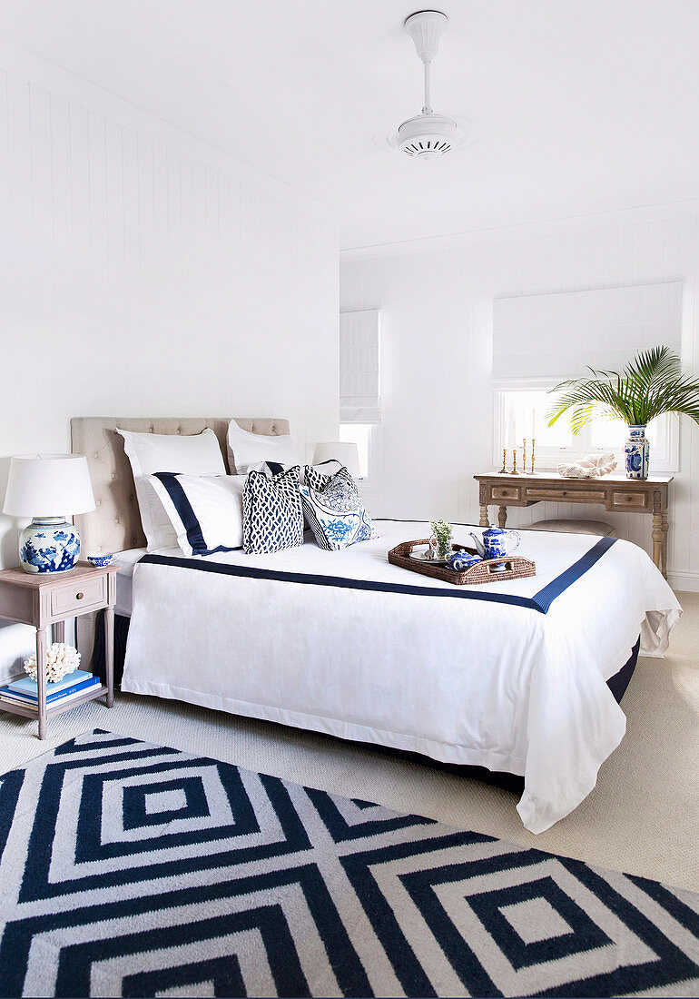 Doppelbett im Schlafzimmer mit weiß-blauen Accessoires, im Hintergrund Antik Konsolentisch
