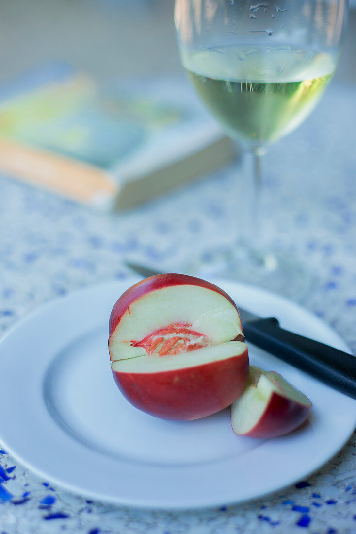 A white nectarine, sliced with a knife on a plate with a glass of white wine