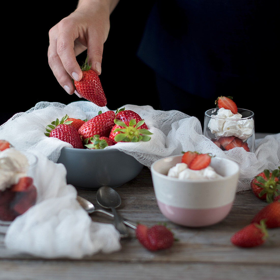 Strawberries with cream and a hand holding a fresh strawberry