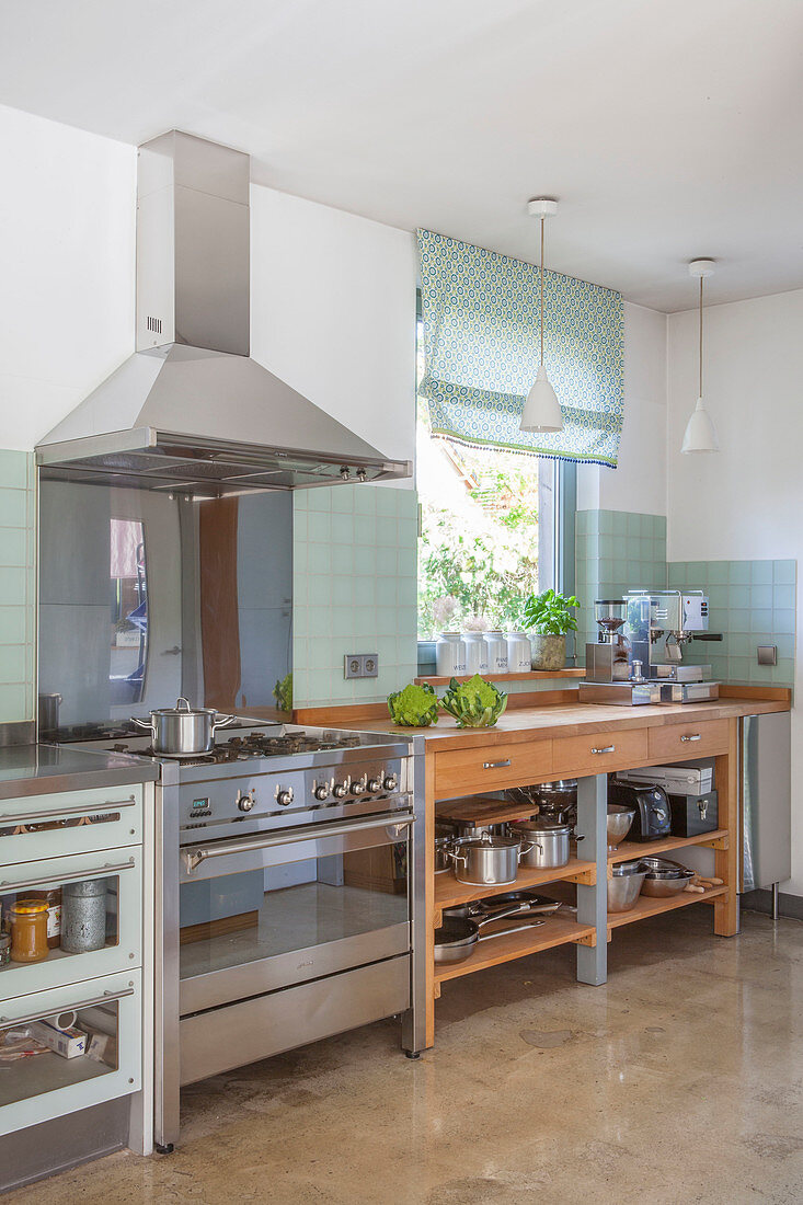 Wooden counter with drawers and open-fronted shelves combined with stainless steel appliances in kitchen