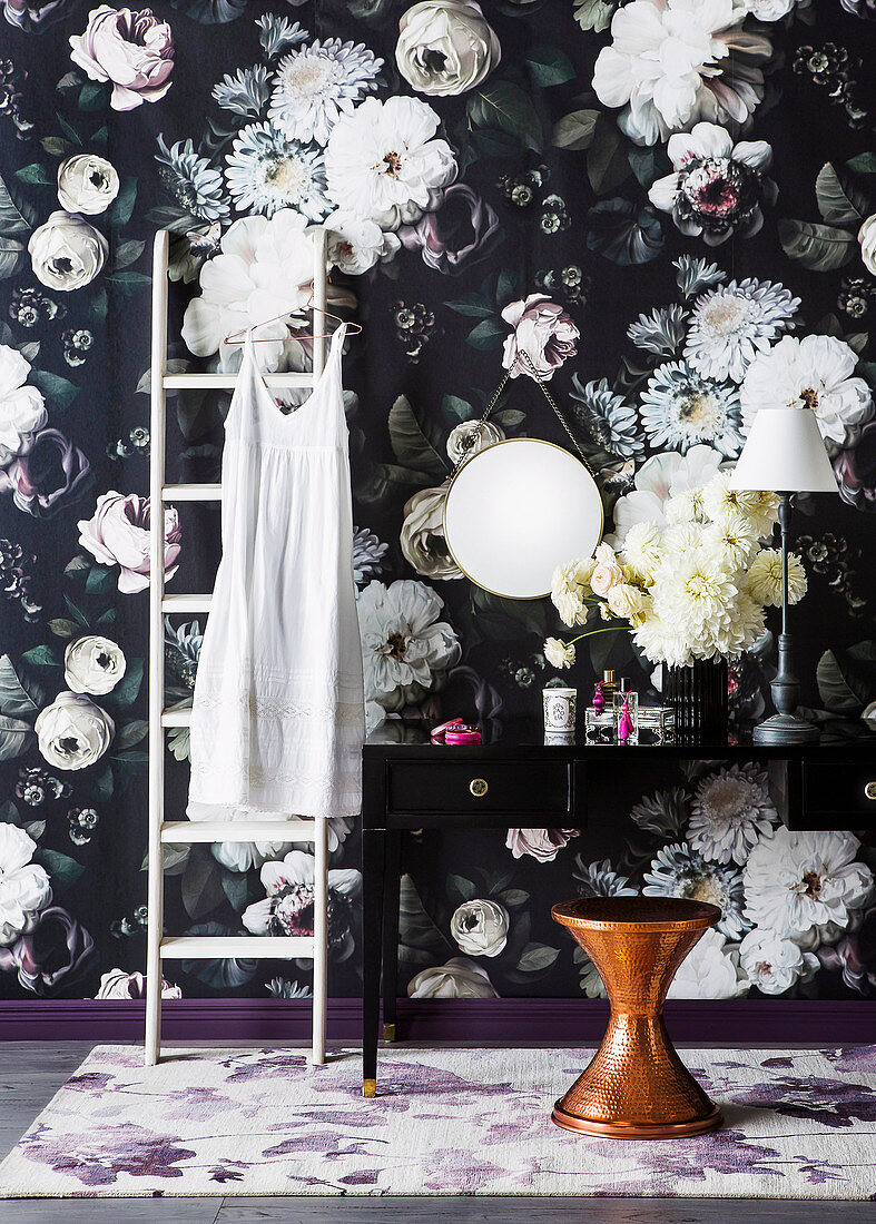 Ladder and dressing table in front of dark floral wallpaper