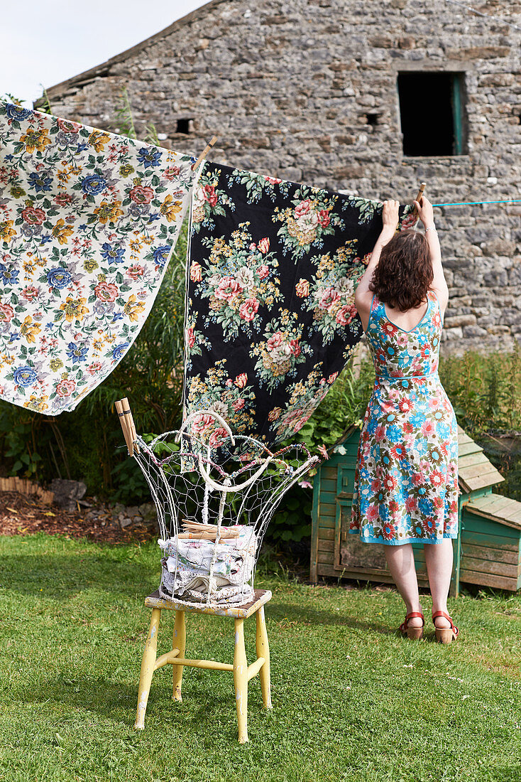 Woman wearing floral dress hanging up laundry to dry in garden