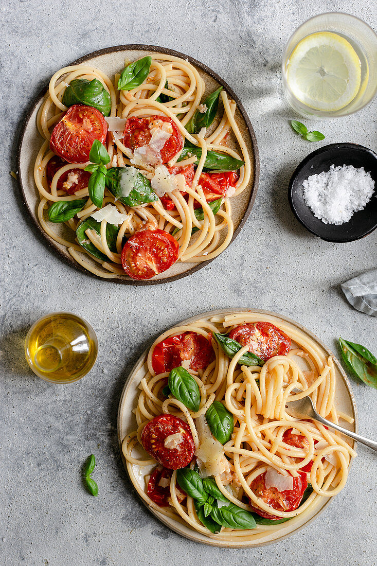 Two plates of bucatini pasta with roasted tomatoes and basil