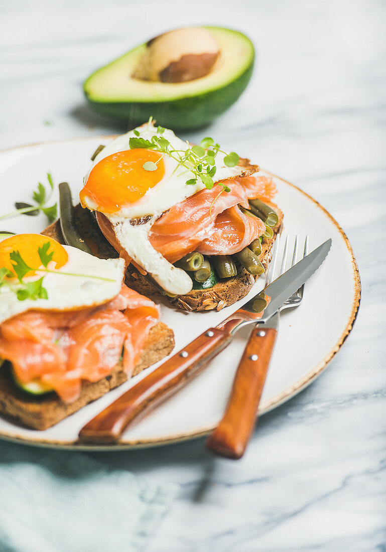 Healthy breakfast sandwich with salmon, avocado, fried egg, sauted green beans and fresh sprouts