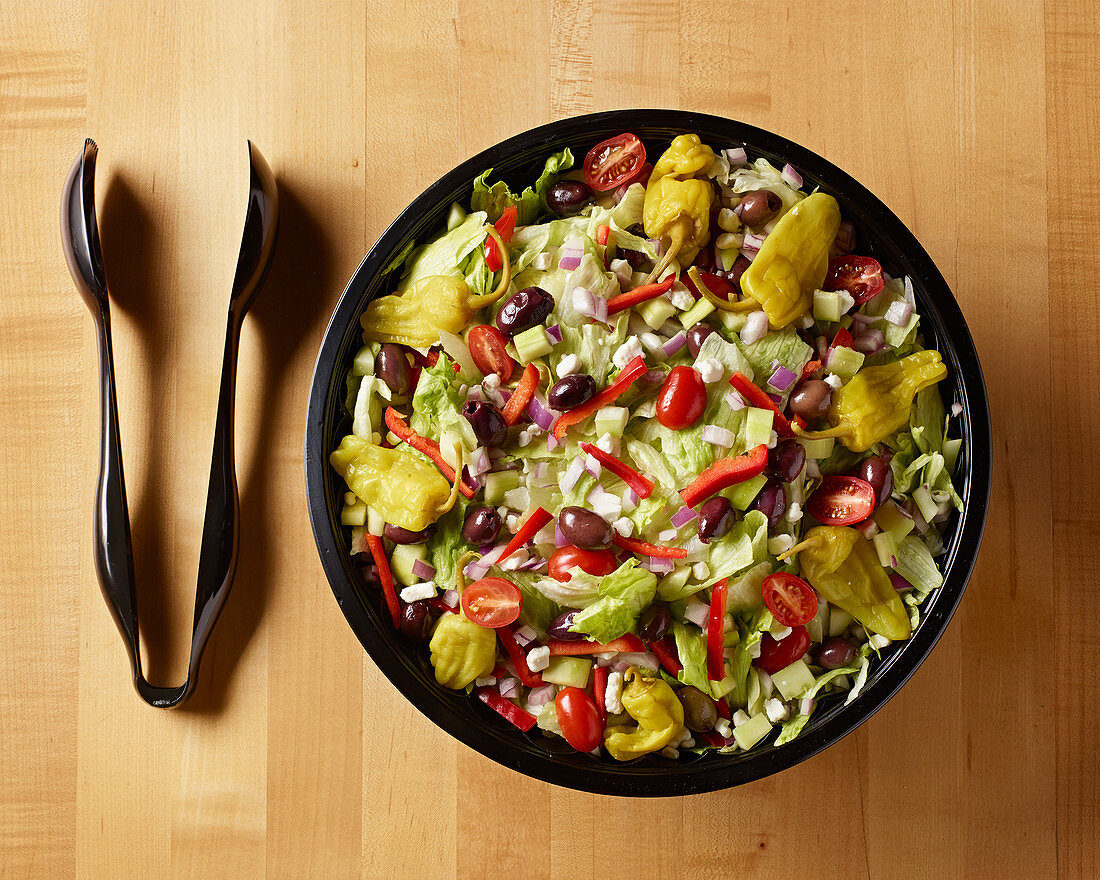 Griechischer Salat in schwarzer Salatschüssel und schwarze Salatzange
