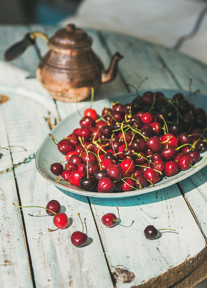 Plate of fresh ripe sweet cherries on rustic light blue wooden garden table