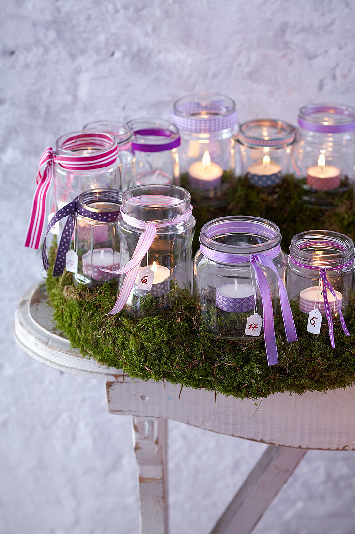 Advent calendar made from tealights jars in moss wreath