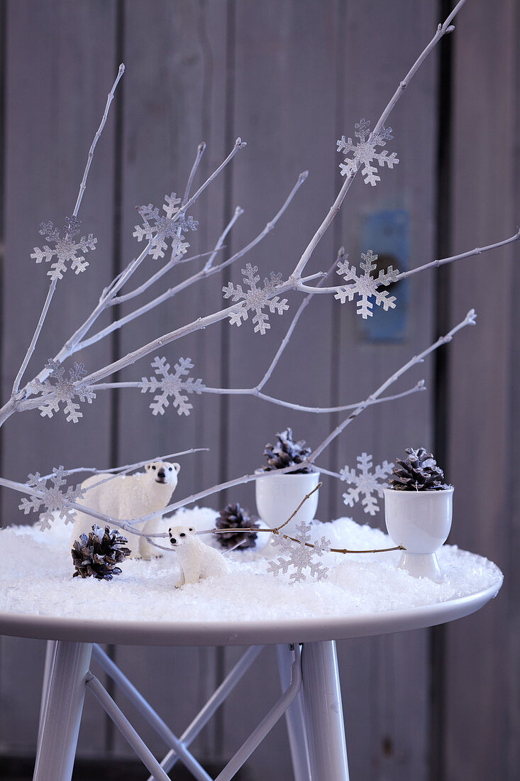 Wintry landscape made from artificial snow, polar bear figurine, pine cones and snowflake decorations on branches