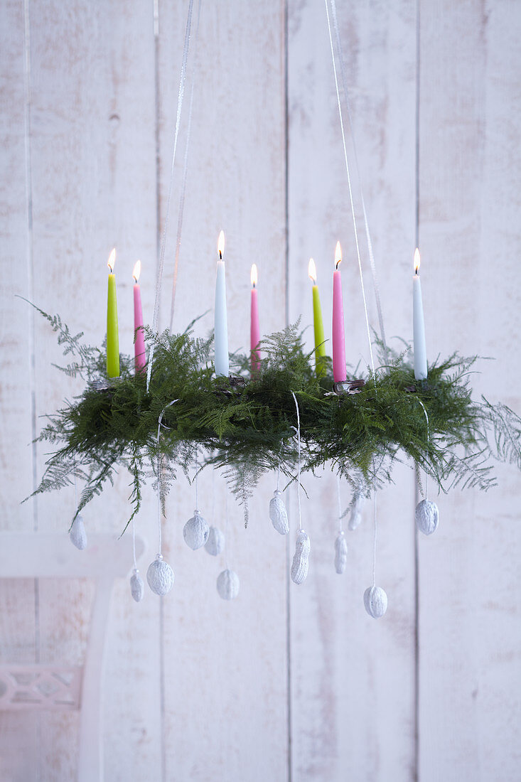 Suspended Advent wreath made from asparagus leaves decorated with candles and white-painted nuts