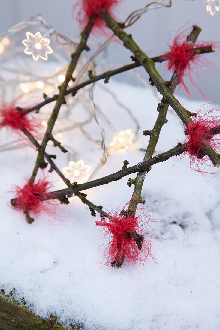 Selbstgebastelter Stern aus Zweigen mit Lichterkette im Schnee