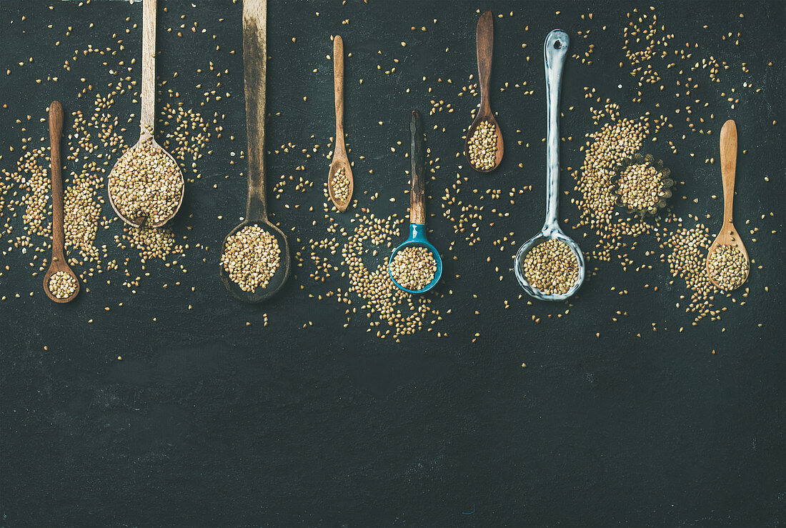 Flat-lay of various old vintage kitchen spoons full of green uncooked buckwheat grains