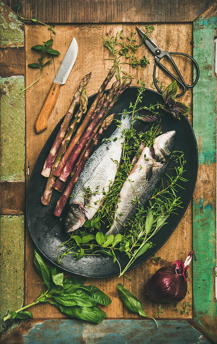 Raw sea bass with herbs and vegetables over rustic wooden background