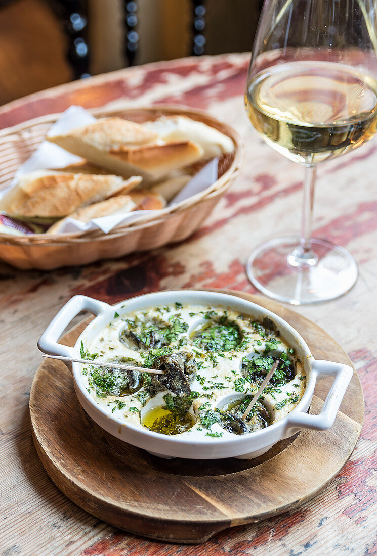 Plate of french escargot snails in a butter sauce with herbs with bread and wine in the background