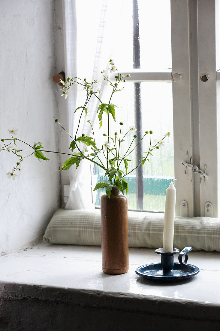 Candlestick and flowering branches in ceramic bottle on windowsill