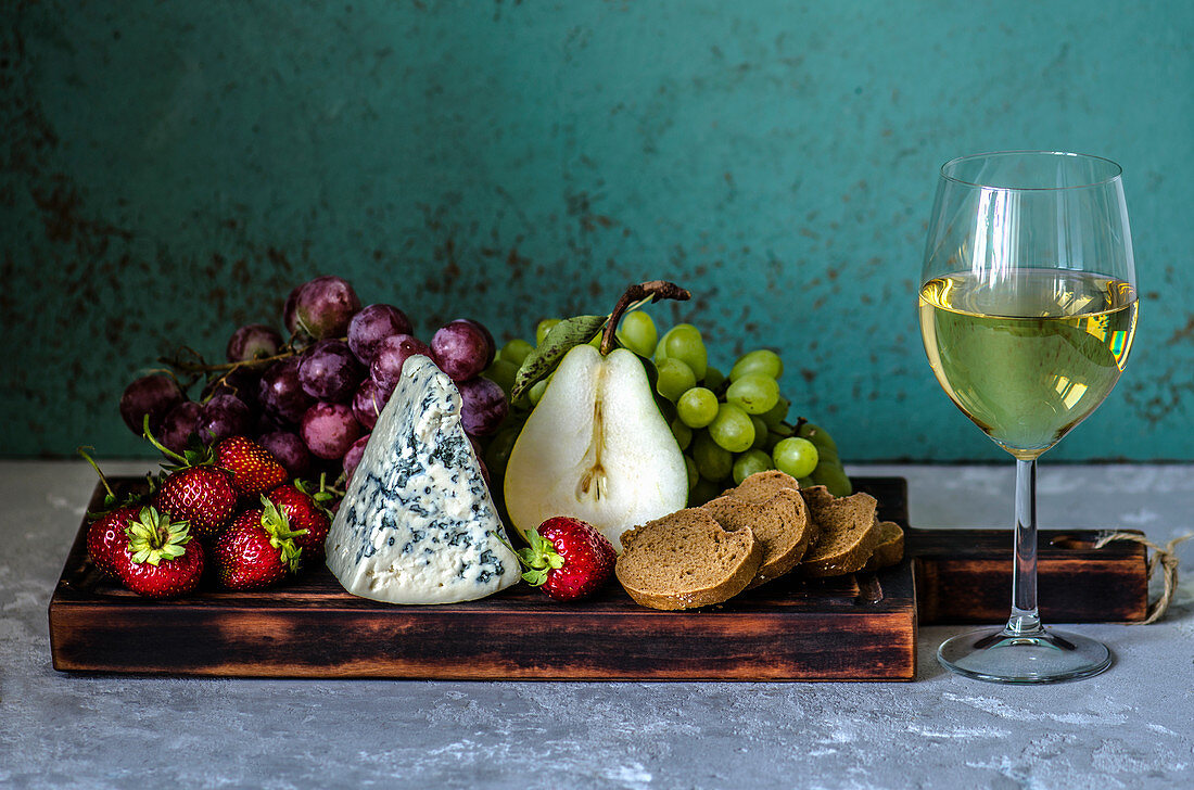 Ein Glas Weißwein, Obst, Blauschimmelkäse und Brot