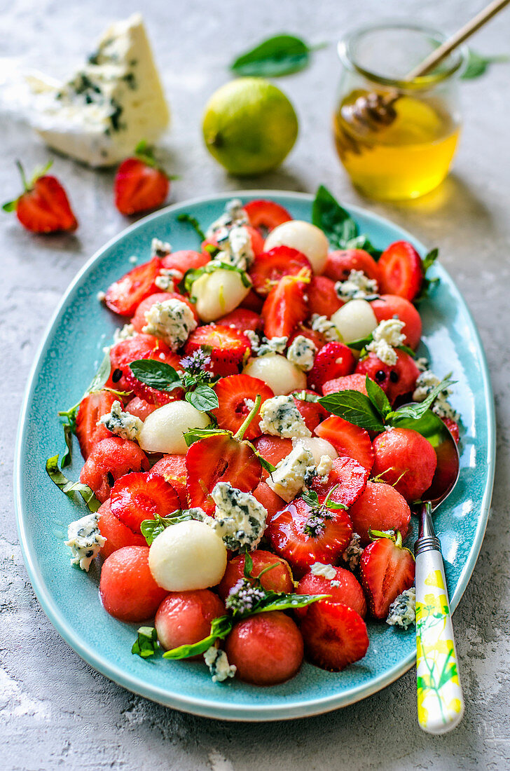 Salad from watermelon, melon, strawberry, basil and blue cheese with honey