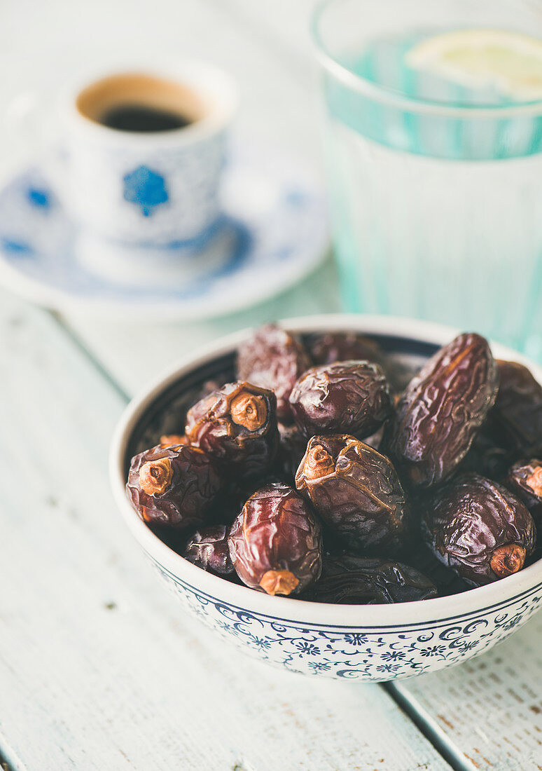 Traditional muslim food for Ramadan iftar meal - Dates, glass of water and coffee over wooden table.