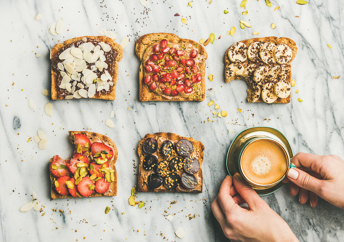 Vegan wholegrain toasts with fruit, seeds, nuts, peanut butter, cup of espresso and woman hands