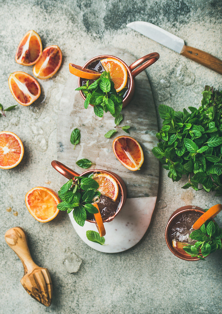 Blood orange Moscow mule alcohol cocktails with fresh mint leaves and ice in copper mugs