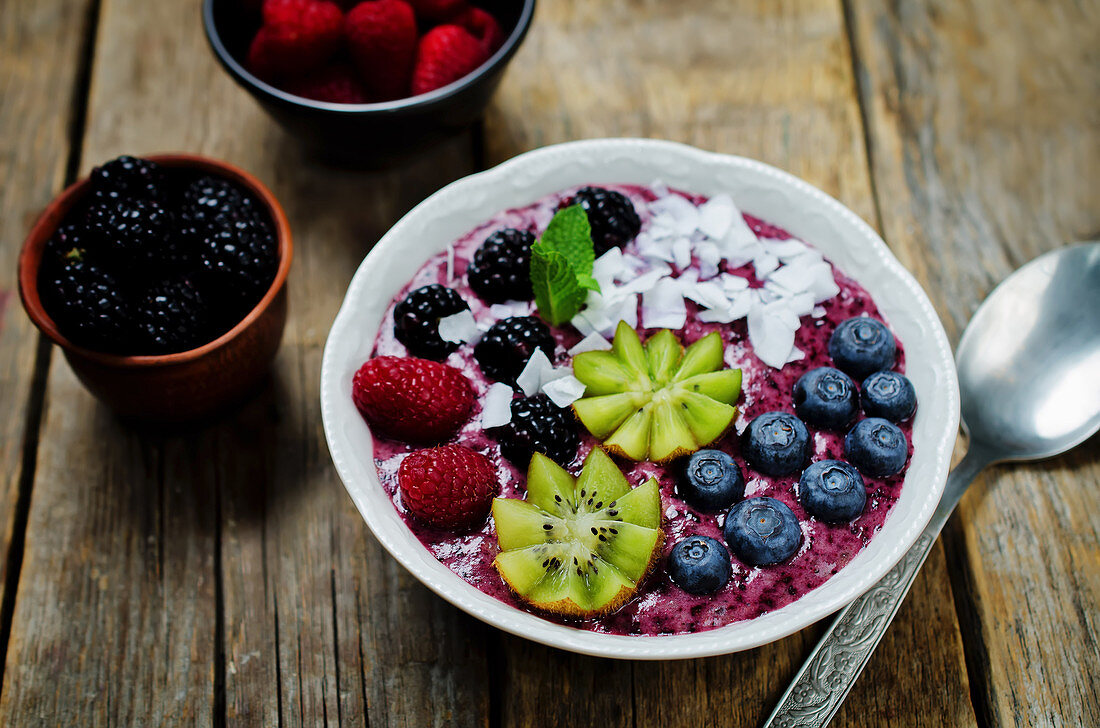 A breakfast bowl with blueberry smoothies, blueberries, kiwi, raspberries, blackberries and coconut flakes