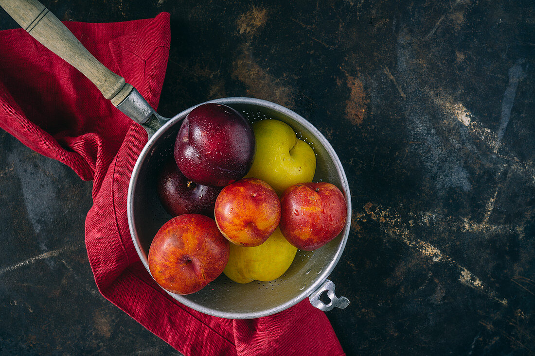 Colourful plums in a vintage sieve