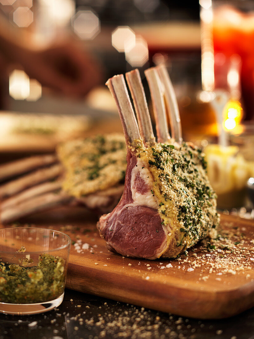 A raw rack of lamb with a herb crust on a chopping board