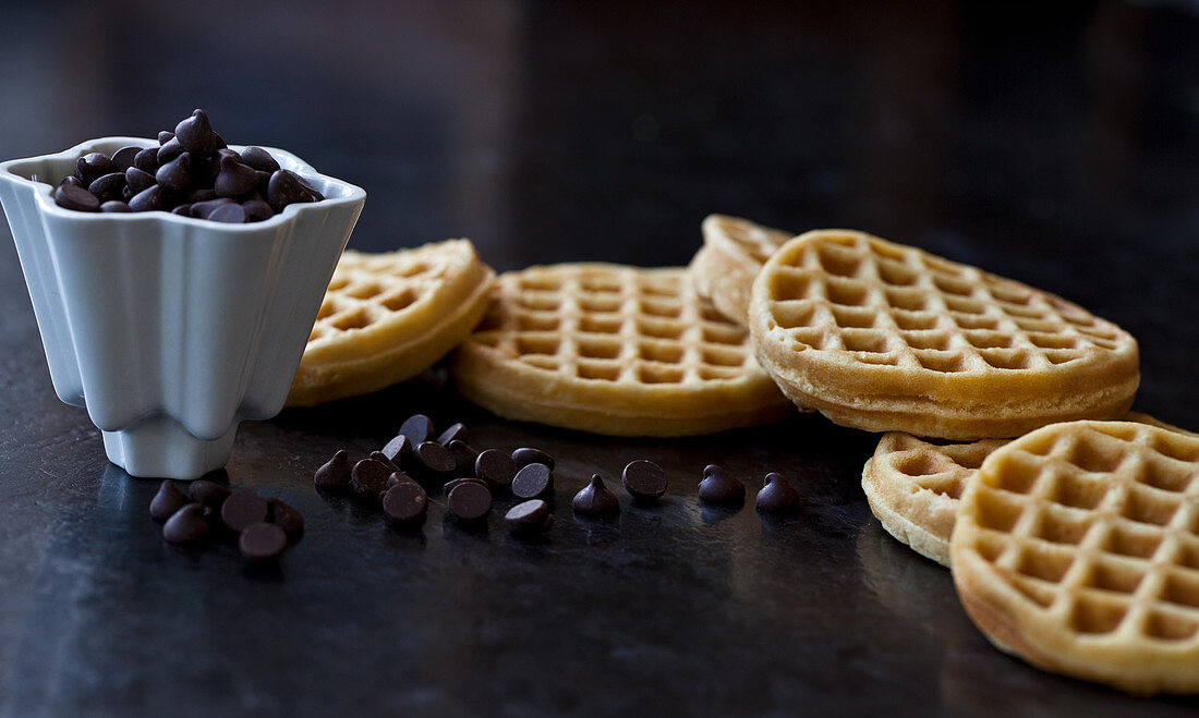 A white bowl with chocolate chips and a stack of homemade waffles