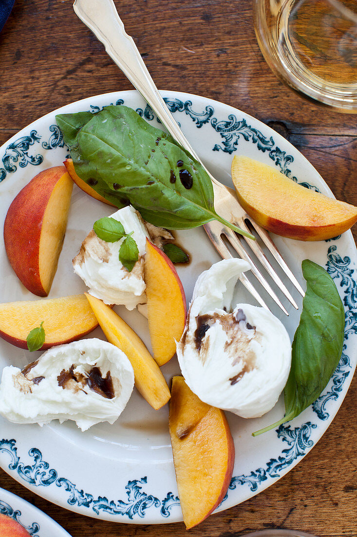 A peach, basil and buffalo mozzarella salad with balsamic and a glass of white wine