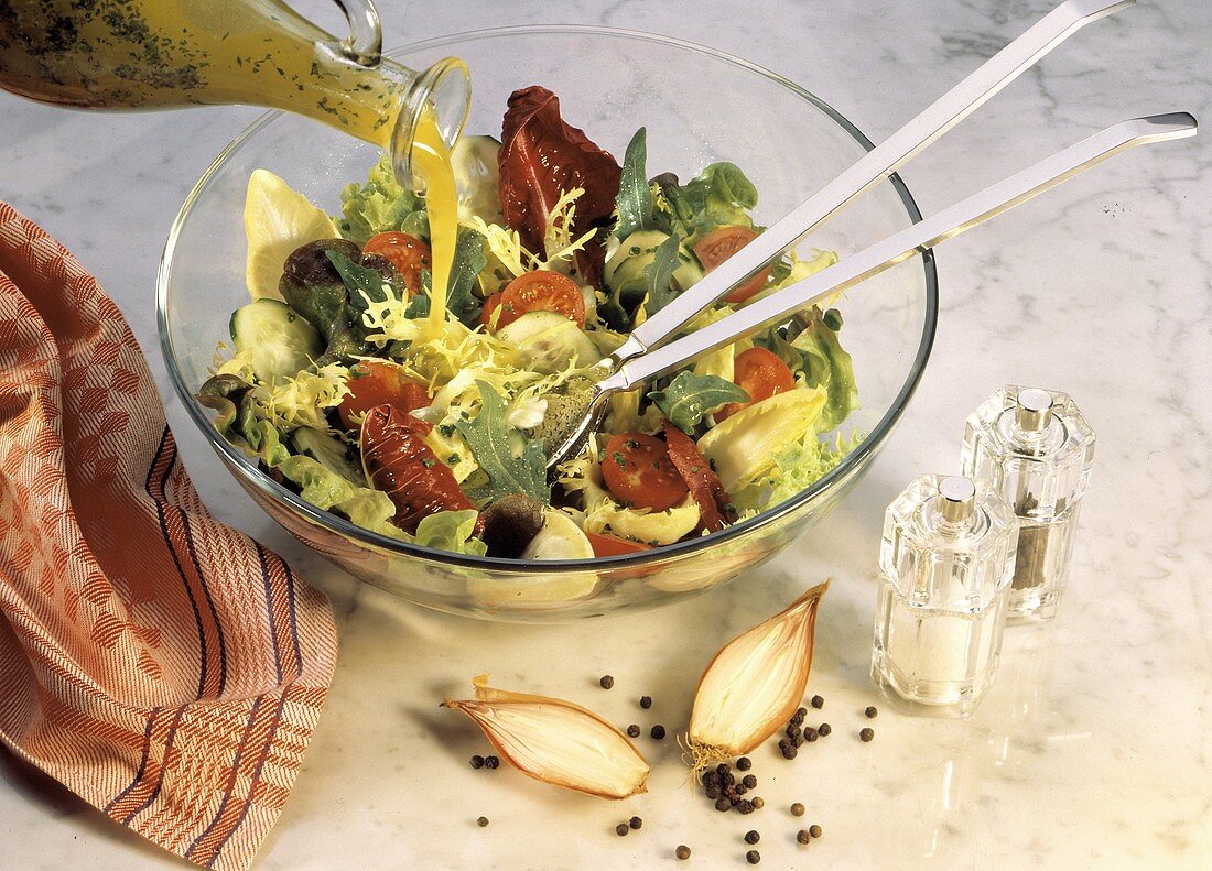 Pouring Dressing over a Mixed Lettuce Salad; Tomatoes