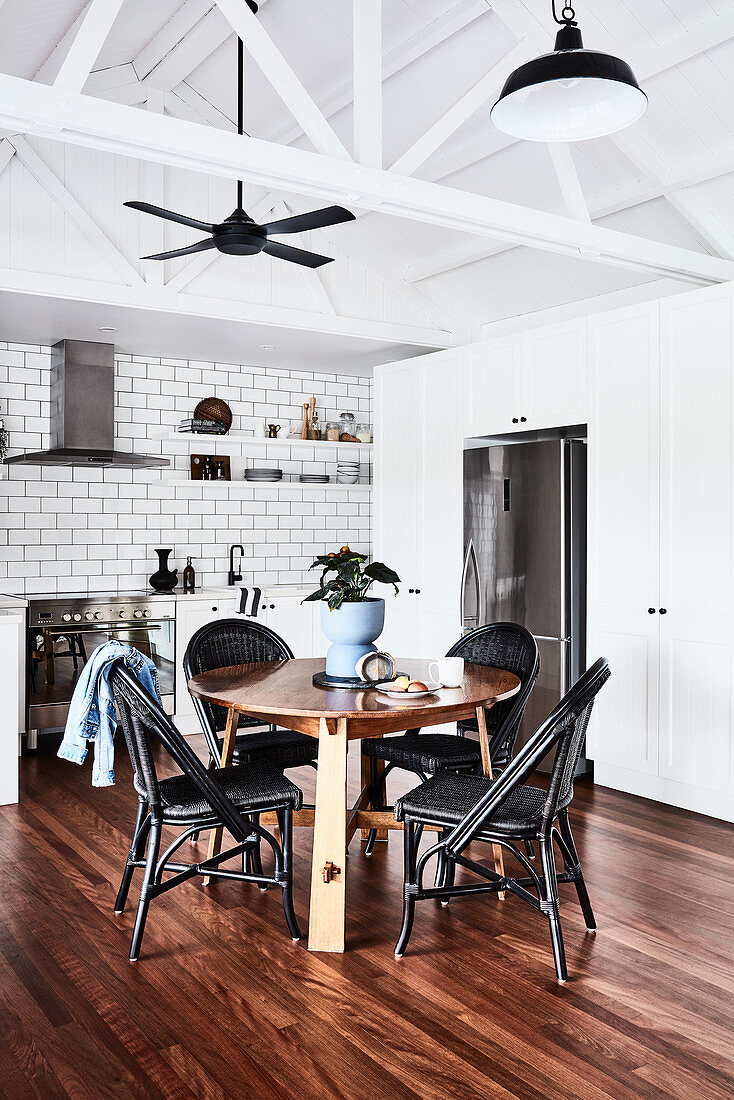 Essbereich mit rundem Tisch und schwarzen Stühlen vor Kühlschrank vor weißer Küchenzeile