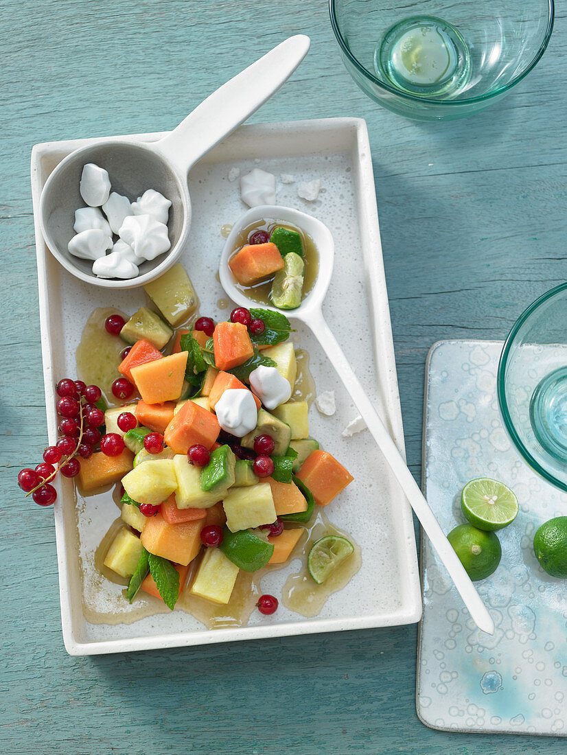 Fruit salad with melon, avocado, pineapple, papaya, redcurrant and ginger meringue dots