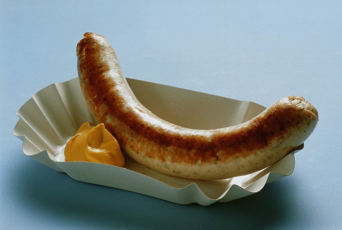 A fried sausage (Bratwurst) with mustard in paper dish